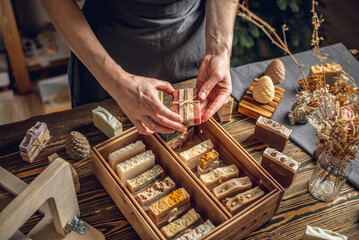 A woman soap maker holds handmade soap in her hands. A lot of different sliced pieces in a wooden...