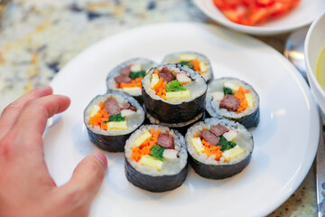 kimbap making, a cherished Korean culinary tradition. Skilled hands roll rice, vegetables, and seaweed, crafting delicious, nutritious bites for an authentic dining experience