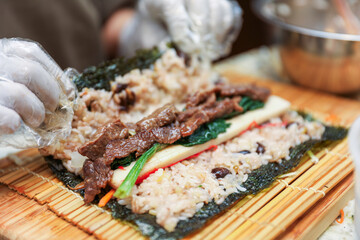 kimbap making, a cherished Korean culinary tradition. Skilled hands roll rice, vegetables, and seaweed, crafting delicious, nutritious bites for an authentic dining experience