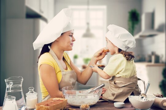 Attractive mother cooking with her cute daughter at home.