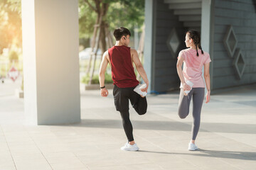 Young Asian couple in sportswear doing stretching together before jogging exercise in urban area....