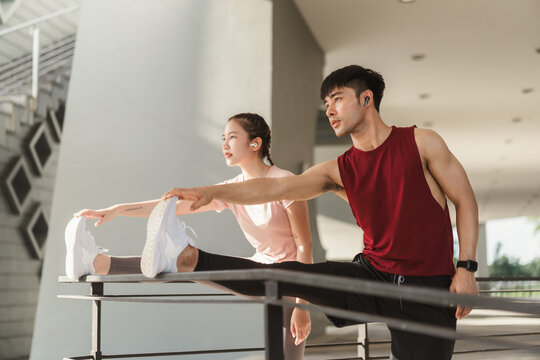 Two Asian young athlete man and woman in sportswear doing stretching together before jogging exercise in urban area. Warming up for workout outdoor in the morning.