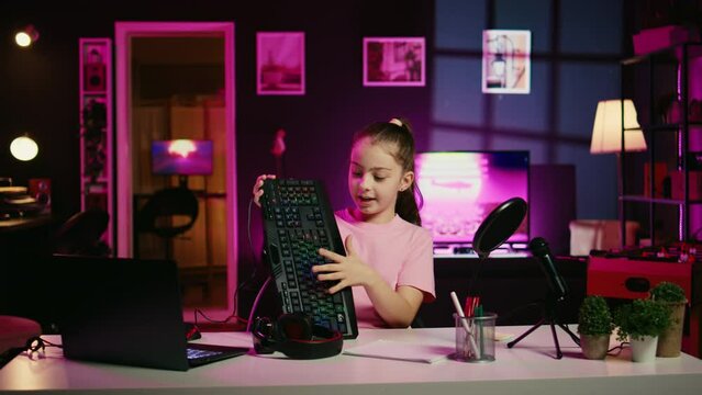 Child influencer filming keyboard, mouse and headphones review in home studio, showing capabilities and specifications. Little girl showcasing computer peripherals to fans on gen Z online channel