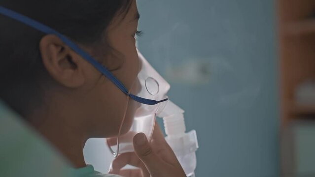 Asian girl having an oxygen mask and breathing through a nebulizer at the hospital.
