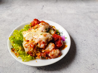 Close up Korean style fried chicken with spicy sauce and mozzarella cheese sprinkled with scallion and sesame seed and lettuce on the side on a white plate.