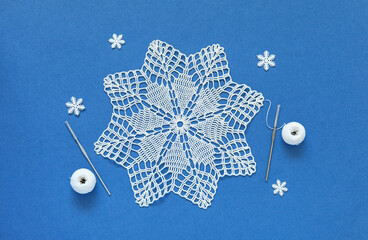 Top view of beautiful hand crocheted lace doily in shape of Christmas snowflake on blue background...