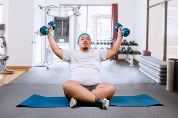 Asian fat middle aged guy exercising using dumbbells in a weight room
