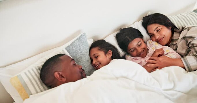 Family, parents and children wake up p in bed from above with love in the morning and relax together. Mother, father and cuddle with kids in the bedroom of home on a weekend, vacation or holiday