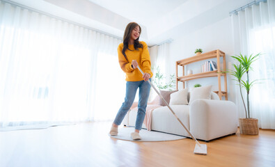 House cleaning with fun. Young adorable asian woman cleaning up living room, using mop as...