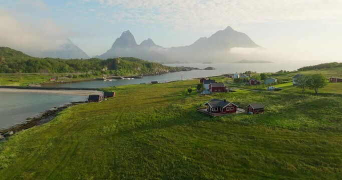 Holdoya village homes on grassy slopes above ocean with jagged mountains wrapped in clouds, Norway
