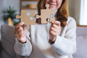 Closeup image of a young woman holding and putting a piece of wooden jigsaw puzzle together