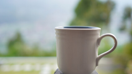 A white cup of coffee or tea object on the table with blur green garden outdoor background. Empty...