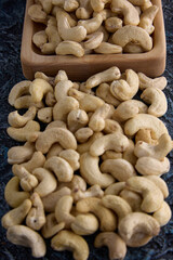 Top view of cashew nuts randomly placed on a textured gray background. Delicious cashew nuts are scattered on the table and in a wooden bowl