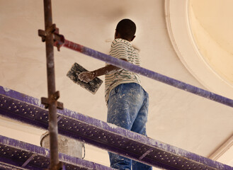 african construction worker climbed on scaffolding plastering a wall