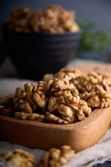 Large peeled walnuts are stacked on a wooden board. Delicious walnuts in a dark interior are scattered on burlap and in a wooden plate.