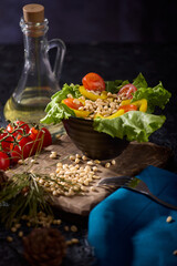 Healthy delicious breakfast of fresh vegetables and cedar kernels. Fresh vegetables from cherry tomatoes, green lettuce leaves and peeled pine nuts are beautifully laid out on dark textured background