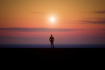 A man stands in an open area and looks at the sunset.