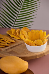 Slices of candied fruit, sweet, healthy yellow mango, neatly arranged on a white plate against a background of green tropical leaves. A neat portion of healthy and delicious mango