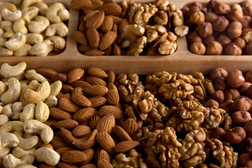A rich nutty assortment of delicious dried and roasted nuts. A mixture of cashews, almonds, hazelnuts, walnuts in a wooden bowl close-up