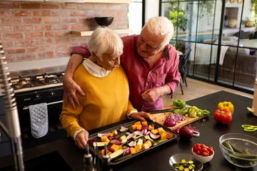 Foto op Plexiglas Happy caucasian senior couple preparing fresh vegetables embracing in kitchen, copy space © wavebreak3