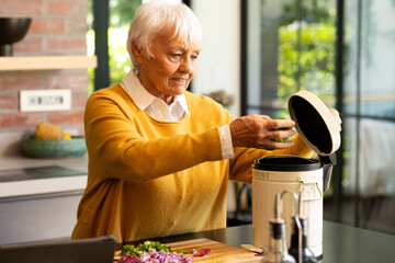 Happy caucasian senior woman preparing food, composting vegetable waste in kitchen