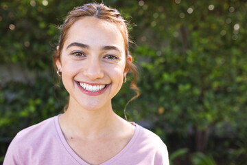 Portrait of happy biracial woman with long brown hair smiling in sunny garden, copy space