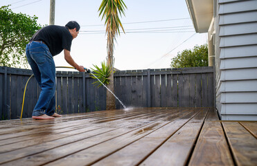 Man washing wooden deck with a water sprayer. Auckland.