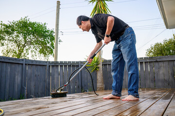 Man cleaning wooden deck with brush and water sprayer.