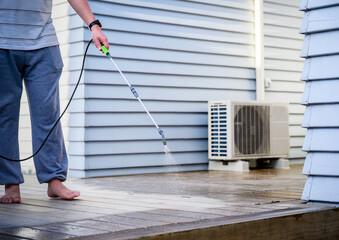 Man cleaning wooden deck with hand-held pressure sprayer, preparing deck before staining.