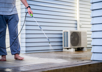 Man cleaning wooden deck with hand-held pressure sprayer, preparing deck before staining.