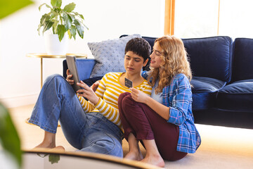 Happy biracial lesbian couple sitting on floor shopping online with tablet and credit card - obrazy, fototapety, plakaty