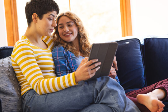 Happy biracial lesbian couple relaxing on couch using tablet together - Powered by Adobe
