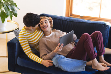Happy biracial lesbian couple relaxing on couch together using tablet at home