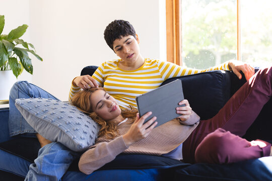 Happy biracial lesbian couple relaxing on couch together using tablet at home