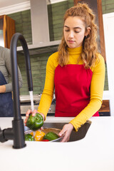Focused biracial lesbian couple preparing food, washing vegetables in kitchen sink