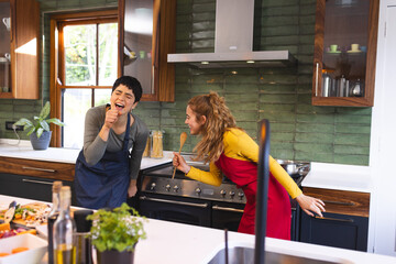 Happy biracial lesbian couple preparing meal having fun singing in kitchen