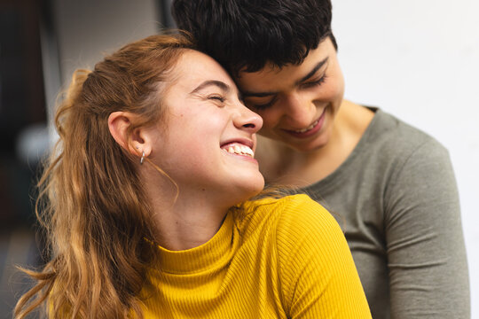 Happy biracial lesbian couple embracing and smiling at home