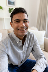 Happy biracial man sitting on sofa having video call at home