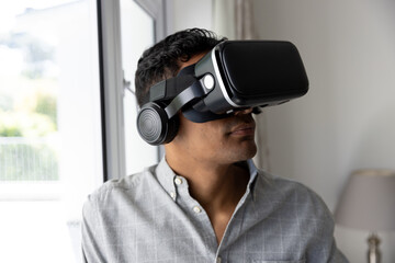 Biracial man using vr headset next to window at home