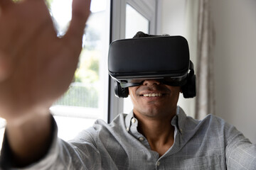 Happy biracial man using vr headset touching virtual screen at home