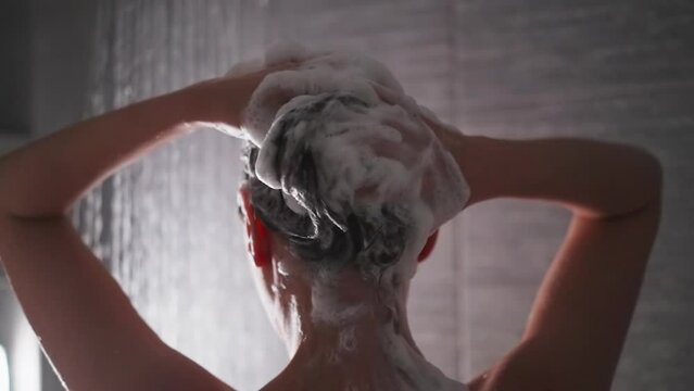 Woman massages foamy hair in shower cabin closeup. Tranquil lady washes hair with shampoo during care procedures in bathroom. Beauty routine