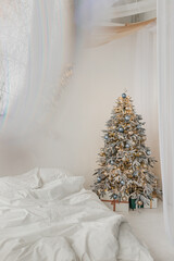 Christmas tree with decorations and lights in a white bedroom. Aesthetics of holiday, relaxation and hygge philosophy.