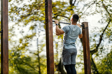 Sportsman doing chin ups in outdoor gym in nature.