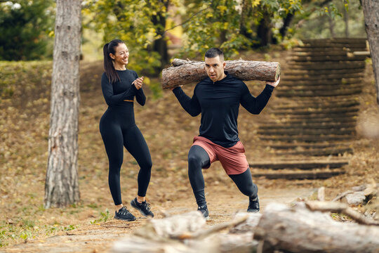 A sportsman is lifting trunk in nature while a sportswoman is supporting him.