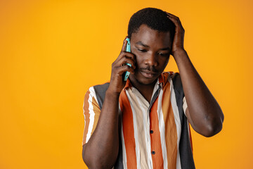 Upset stressed african man talking on the phone against yellow background - obrazy, fototapety, plakaty