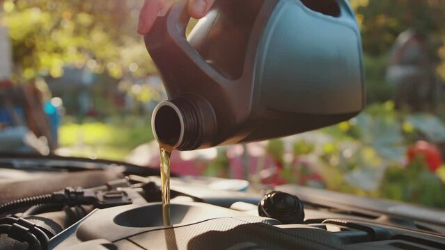 pouring motor oil into the engine against the backdrop of the sun. Additives and tolerances in motor oil, close-up. Slow motion, industry
