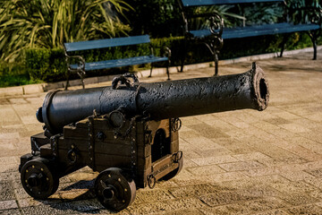 Old bronze cannon on a wooden cart with wheels stands on the paving stones near the bench