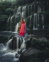 Woman with violin at waterfall in tropical forest. Music and art concept. Female wearing long red...