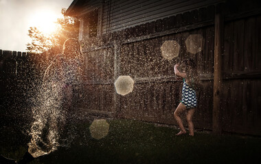 Sisters playing in sprinkler in yard - obrazy, fototapety, plakaty