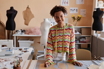 Young smiling craftswoman in casualwear standing by workplace in studio of fashion design or...